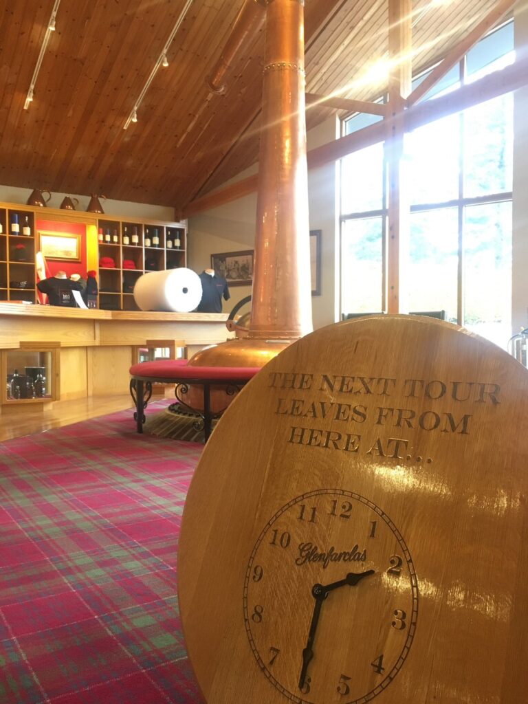 グレンファークラス蒸留所のロビーに置かれた、ポットスチルを模した暖炉のような美しいオブジェ。背景の大きなガラス窓からは、パノラマに広がる緑豊かなお庭が見える