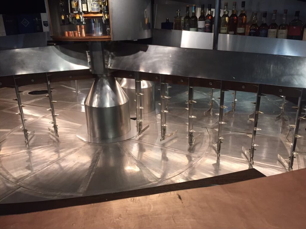 ブレアソール蒸留所のビジターセンター内「マッシュ・タン・バー」で。クライヌリッシュ蒸留所で使われていた巨大な銅製・鋳鉄製の糖化槽を再利用(アップサイクル)した、世界でも類を見ないテイスティングバー。オリジナルのウェッジワイヤー・フィルタープレートの床や、ラウターアームの動きを模したディスプレイなど、ウイスキー製造の歴史を肌で感じられる空間。筆者撮影