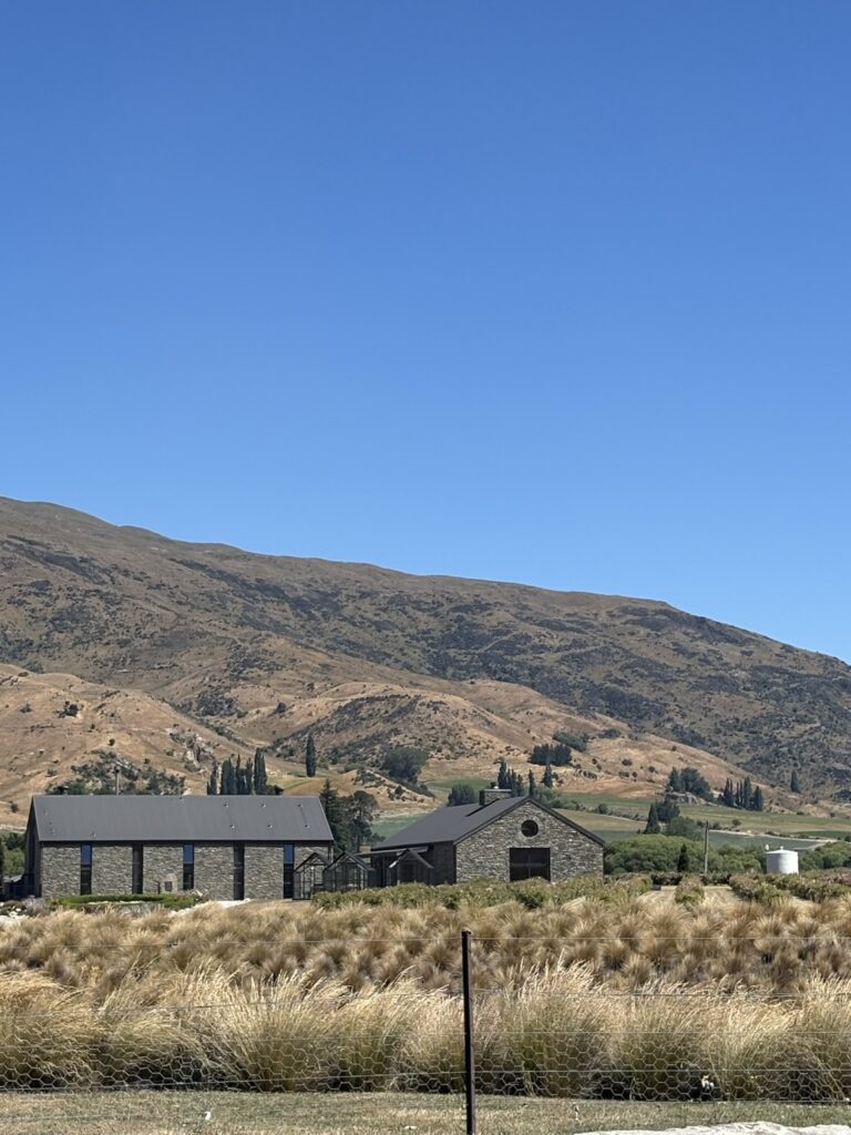 ニュージーランドの青空の下、パドロナ山脈を背景に佇むカルドロナ蒸留所の外観。スコットランドの農家をイメージした石造りと天然木の温もりある建物。