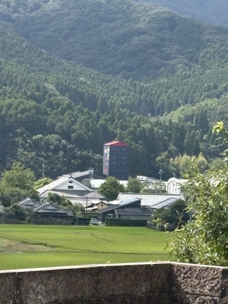 山あいの田んぼの向こうに見えるマルス津貫蒸溜所の旧蒸留塔